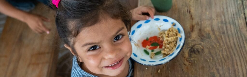 Un niño sonriendo sentado a una mesa con un plato de comida