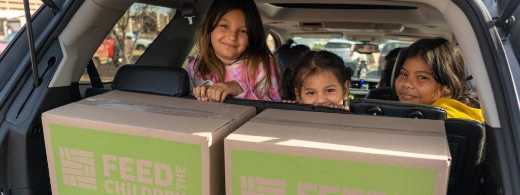 Niños en la parte trasera de un coche con cajas de alimentos