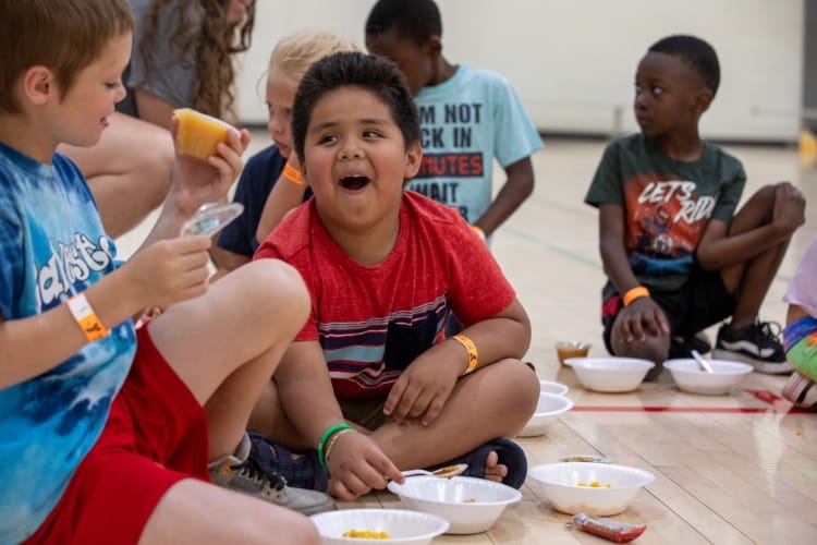 A boy smiling while eating a snack in a school gym