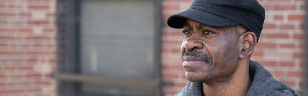 Un hombre con jersey y sombrero delante de una casa