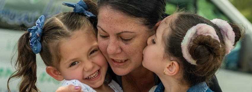 A mother and her two children hugging each other outdoors