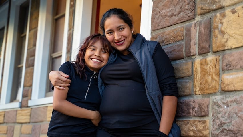 A woman and her daughter hugging outdoors next to a wall