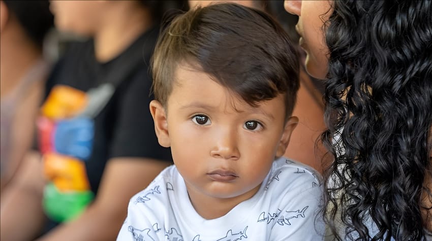 A boy staring at the camera sitting with an adult.