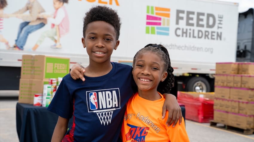 Two children hugging at an outdoor event with boxes