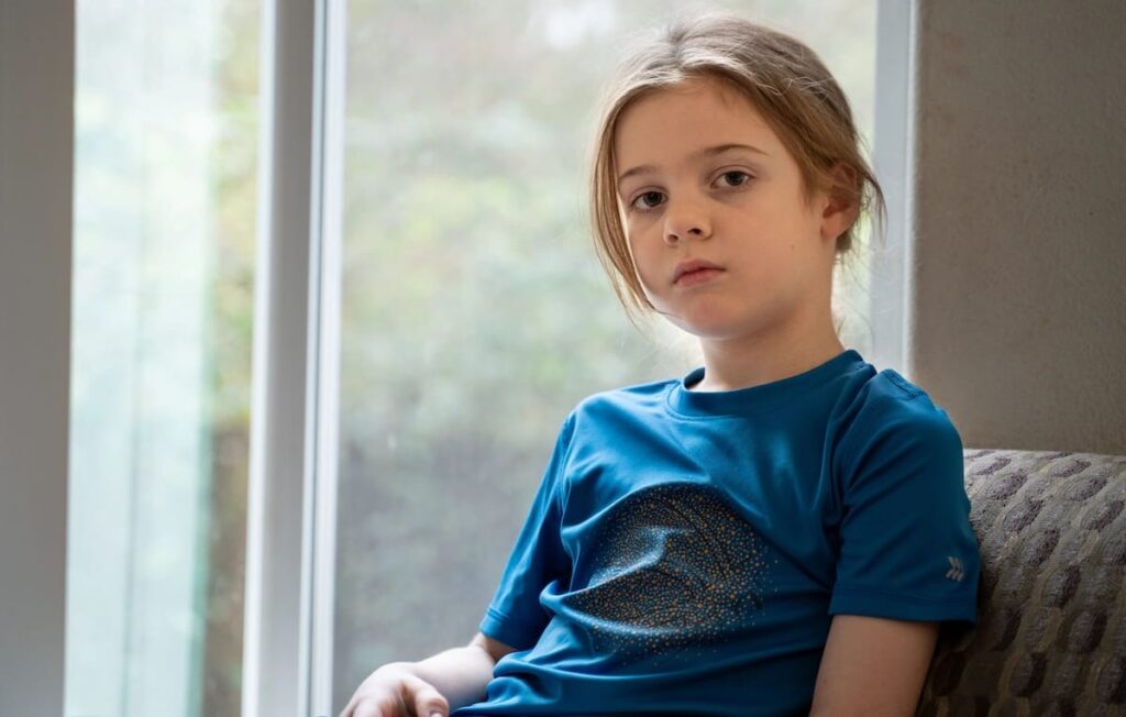 Una chica sentada en una silla junto a una ventana