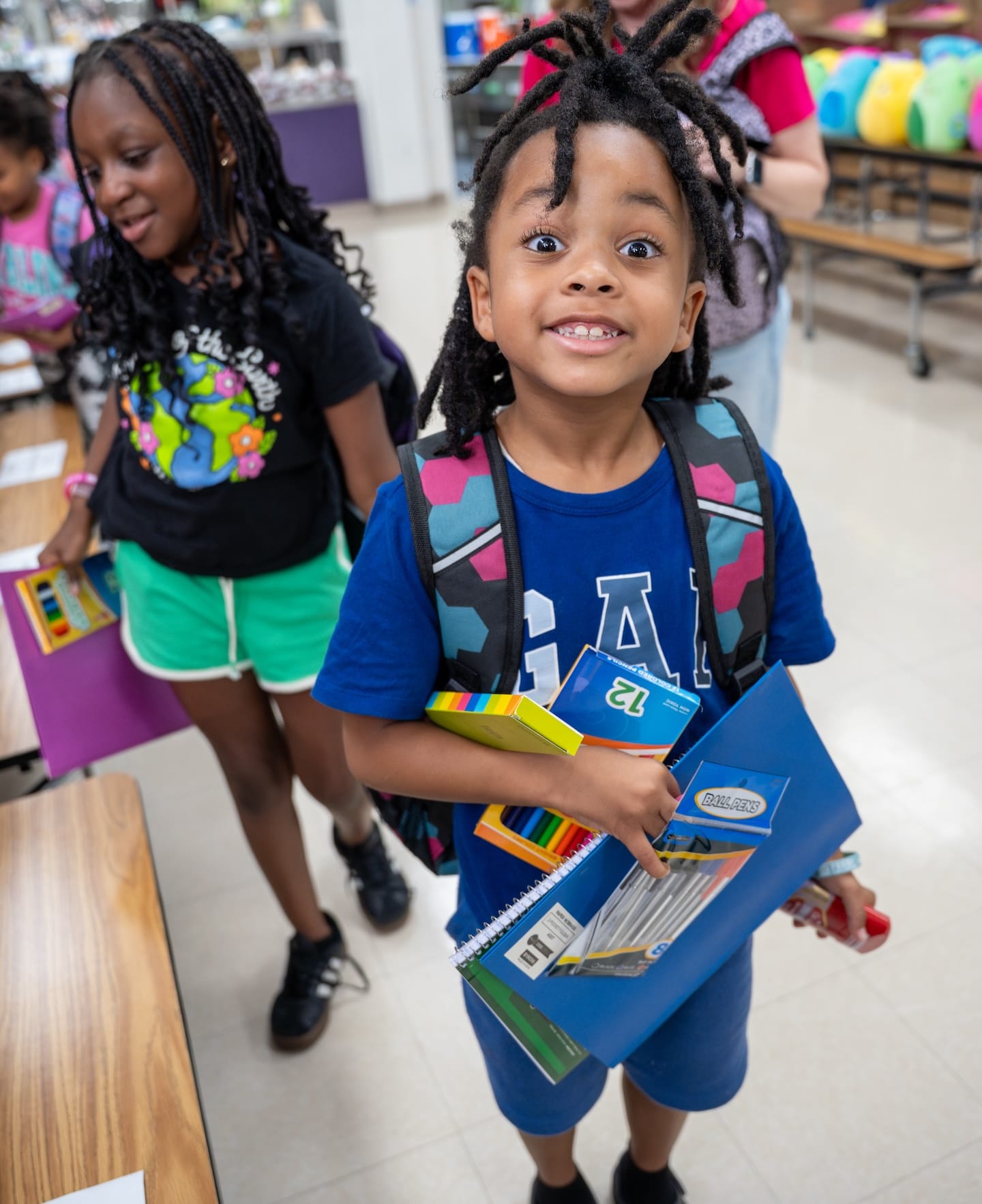 Dos niños de pie con material escolar en una escuela.