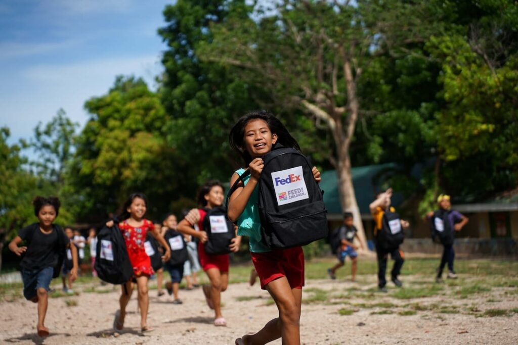 A group of children running while holding Feed the Children backpacks