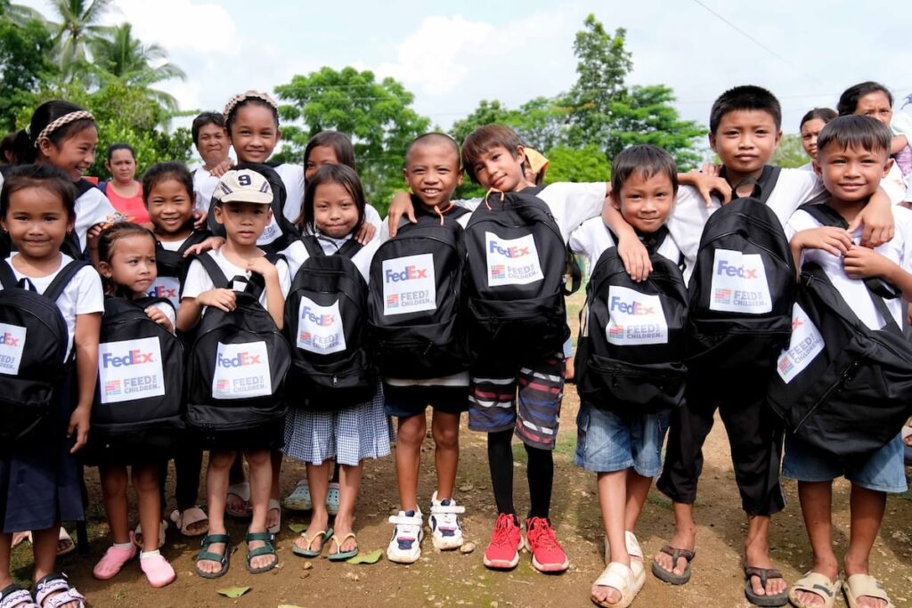 A group of kids holding Feed the Children backpacks outdoors