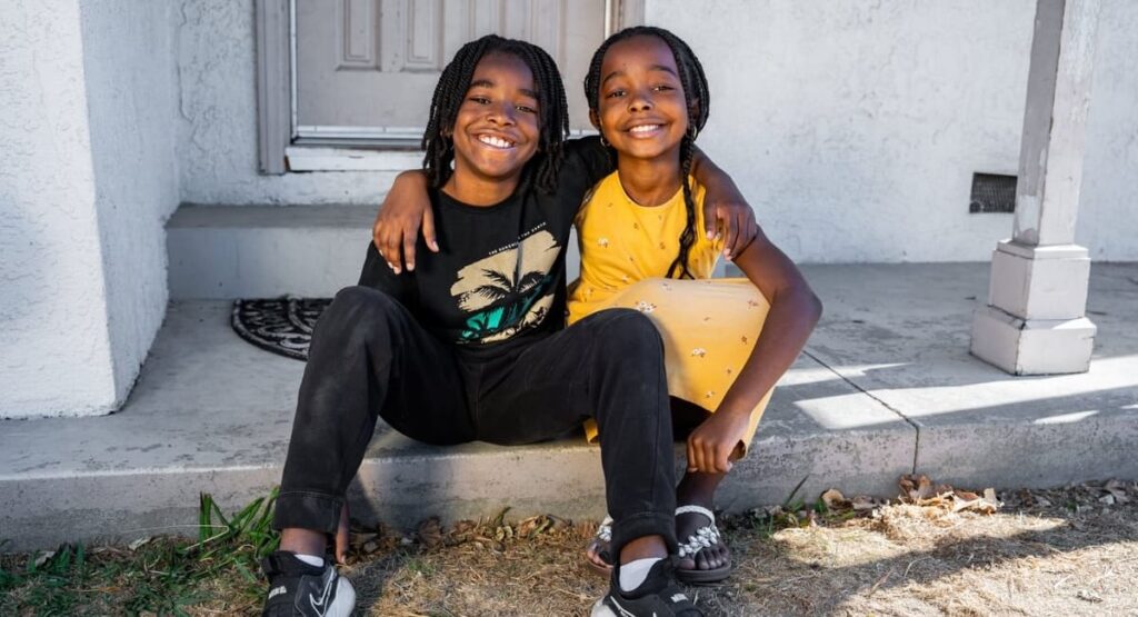 Un hermano y una hermana se abrazan sentados en un porche