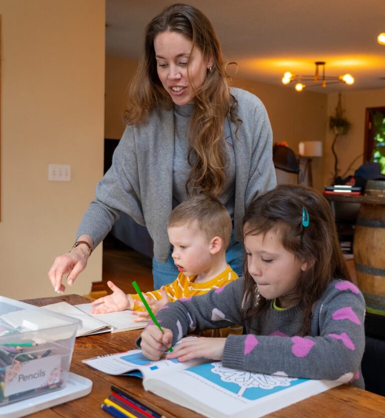 Una mujer con sus dos hijos en una mesa con material escolar.