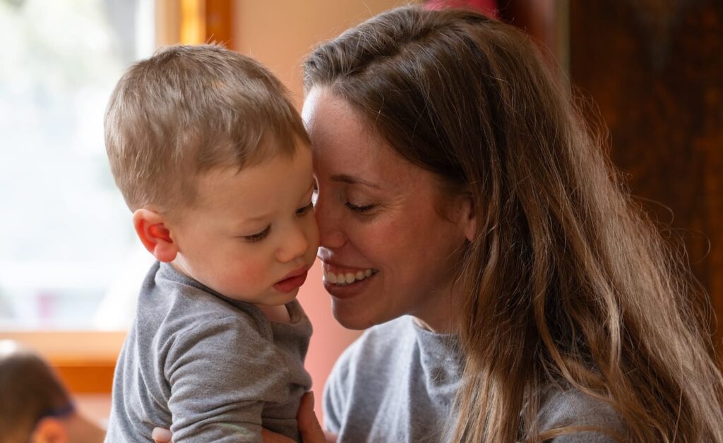 Una mujer con su hijo en brazos mientras sonríe en el interior.