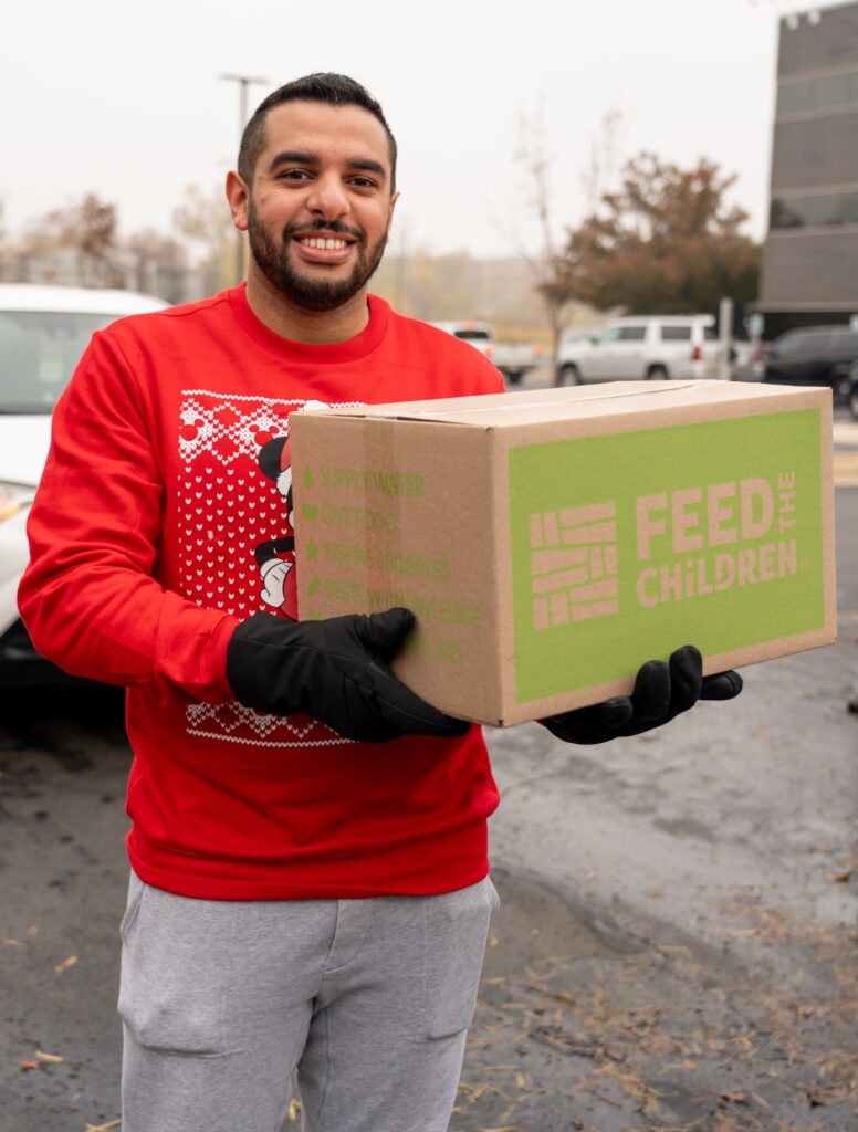 A man holding a Feed the Children box at an outdoor event.