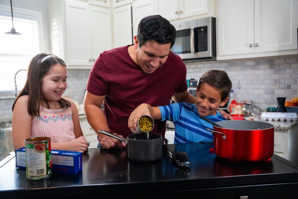 A Dad and his kids in a kitchen cooking.