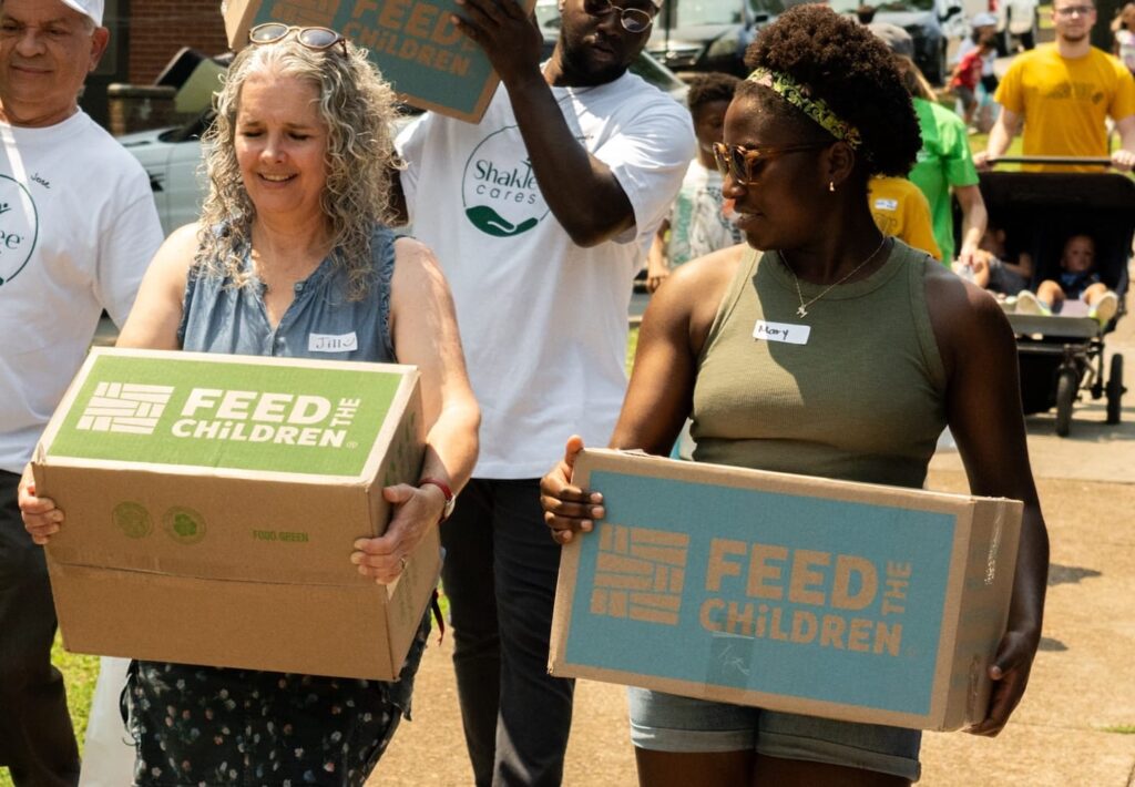 Dos mujeres cargando cajas en un evento al aire libre.