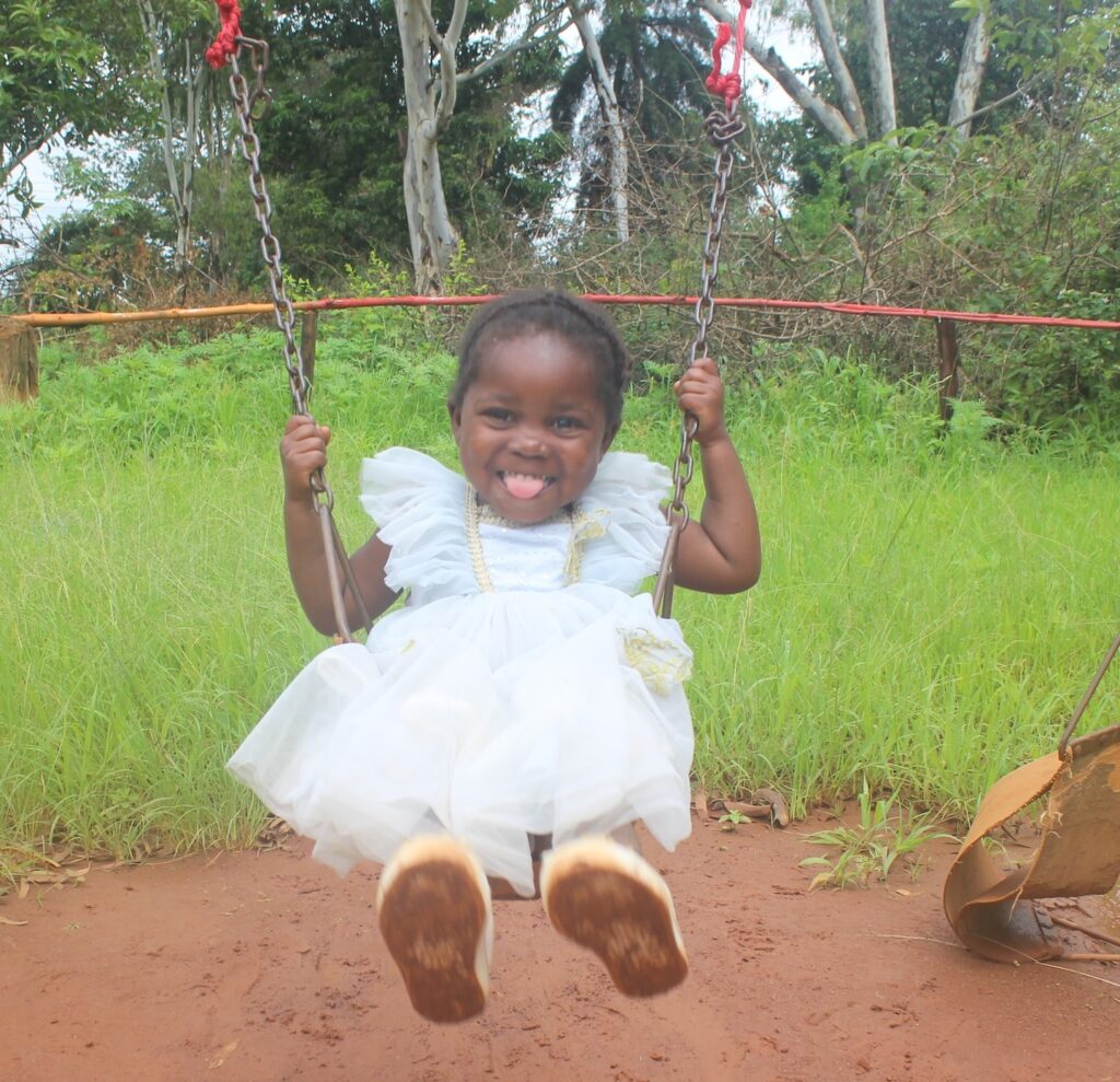 Ackness smiling and swinging on a swingset outdoors.
