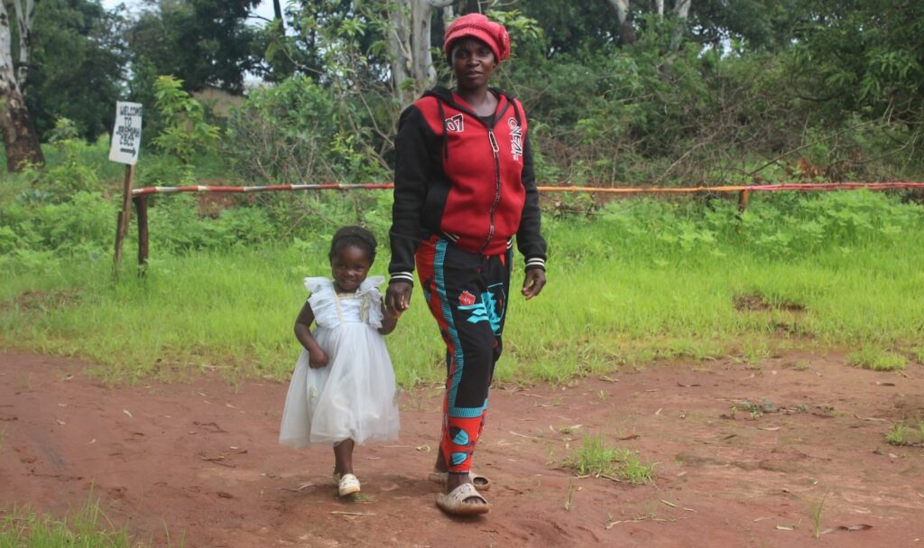 Catherine y Ackness caminando por el camino de tierra frente al bosque.