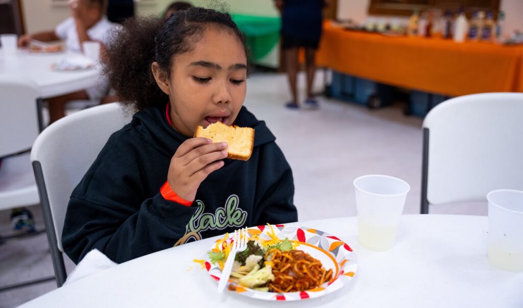 A girl eating a sandwich in a school cafeteria.