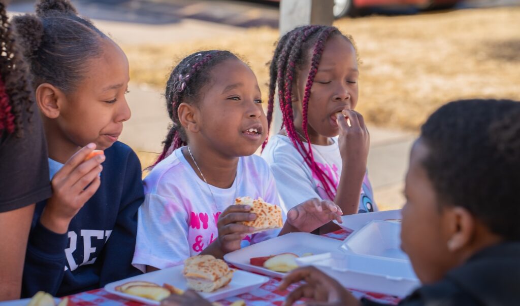 A group of children eating at a table outdoors.