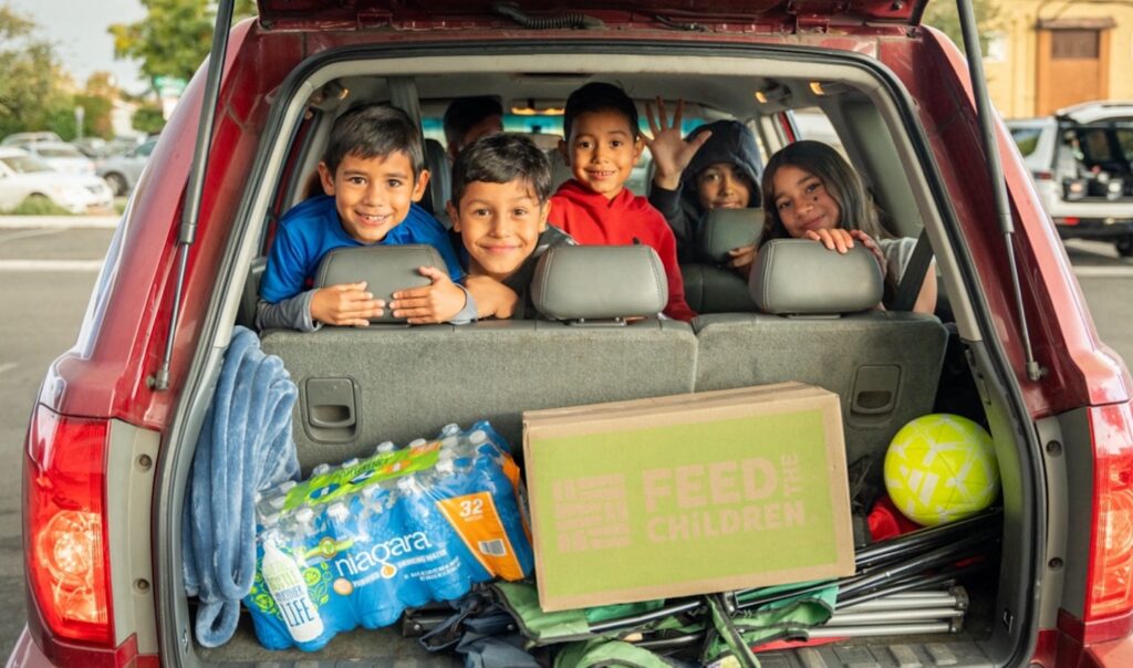 A group of children smiling in the back seat of a car.