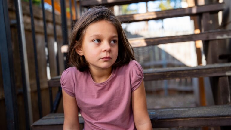 A young girl in a pink shirt sitting on stairs outdoors.