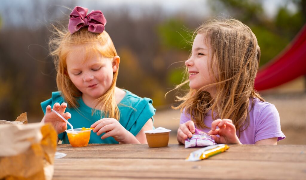 Dos niñas comiendo copas de fruta en una mesa al aire libre.