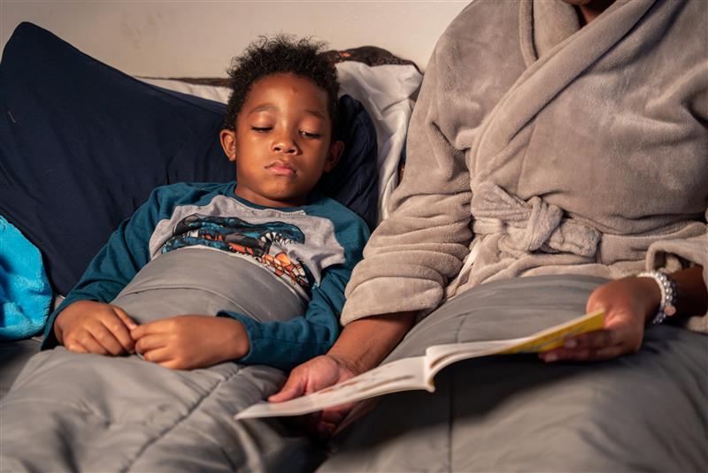 A boy laying in bed next to a parent.